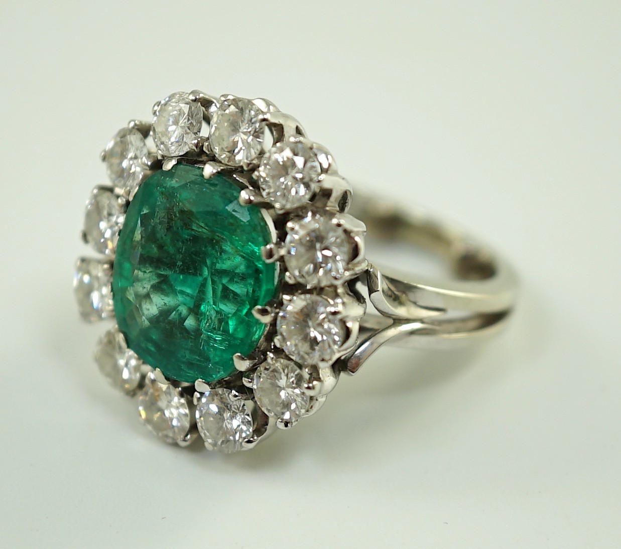 An impressive platinum, emerald and diamond set oval cluster dress ring